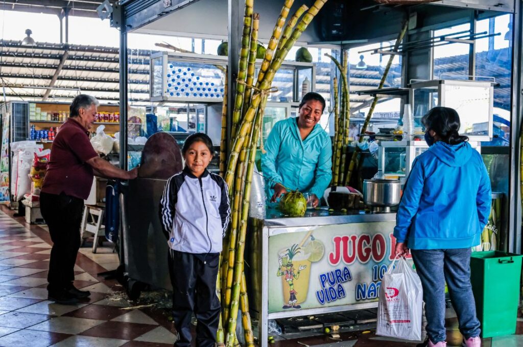 Donna sorridente al banco di un mercato in Ecuador con la figlia, sostenuta da progetti di microcredito internazionale di Banca Etica e Cresud.