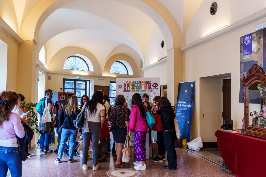 Partecipanti alla Biennale della Prossimità riuniti nel foyer del teatro a Napoli davanti al pannello “Prossimità 2024”