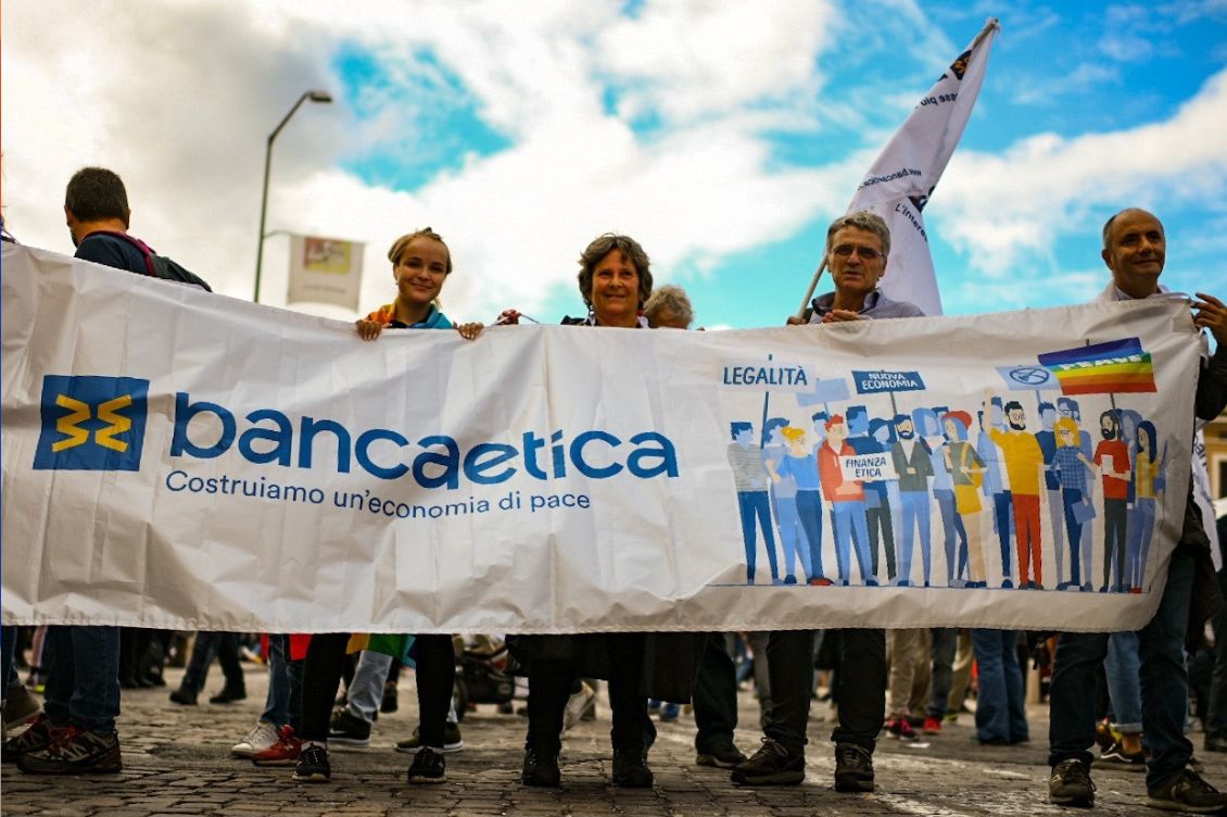 Striscione di Banca Etica alla marcia della pace Perugia–Assisi con persone che sostengono un’economia di pace contro la violenza economica