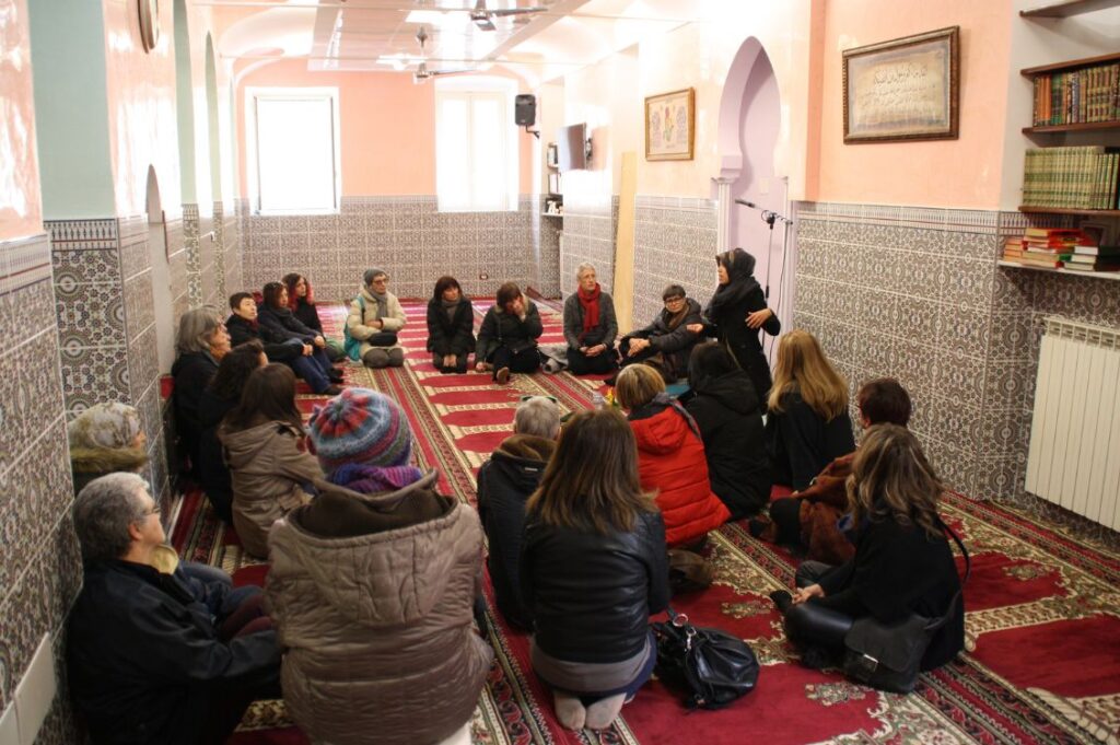 Partecipanti a un Migrantour a Torino seduti sul tappeto di una moschea mentre ascoltano il racconto di una donna della comunità musulmana