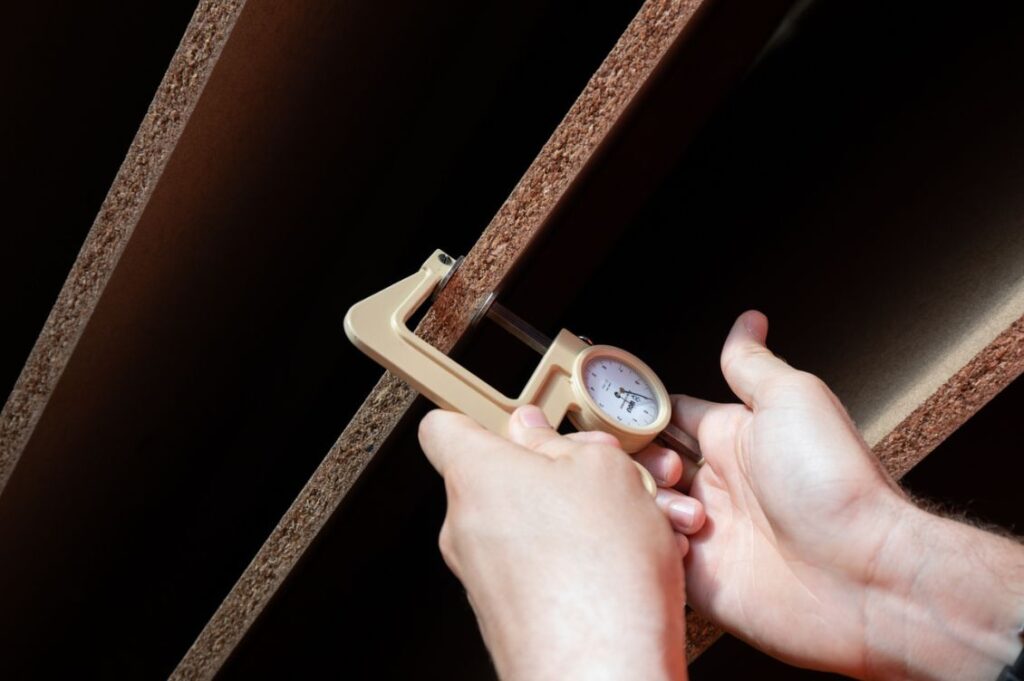 Misurazione dello spessore di un pannello in legno post-consumo durante una fase di controllo qualità